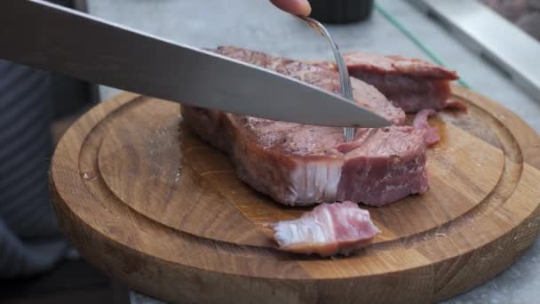 Közelkép egy szaftos, frissen grillezett steakről, amit egyenesen a grillből vágnak le villával és késsel a konyhaasztalon. - Felvétel, videó