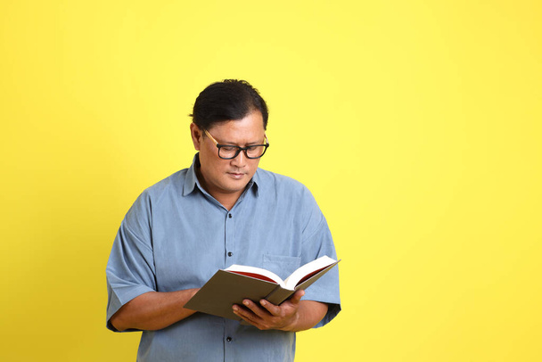 The adult Asian man with blue shirt standing on the yellow background. - Foto, imagen