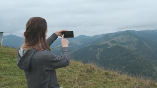Mujer dispara montañas en el teléfono inteligente. Sonriendo, fotografiando picos, cielo, nublado, felicidad, paz. Recreación activa, se encuentra en la parte superior. Cárpatos, Ucrania. Imágenes de alta calidad 4k - Metraje, vídeo