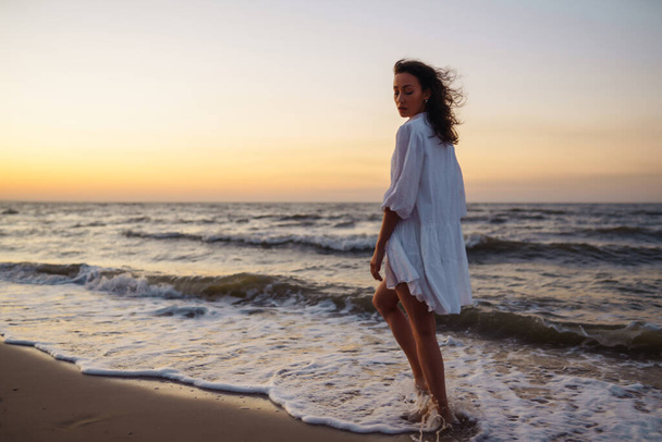 Stylish woman in elegant white dress posing near the sea. People, freedom, lifestyle, travel and vacations concept. - 写真・画像