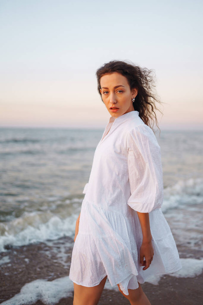Stylish woman in elegant white dress posing near the sea. People, freedom, lifestyle, travel and vacations concept. - Φωτογραφία, εικόνα