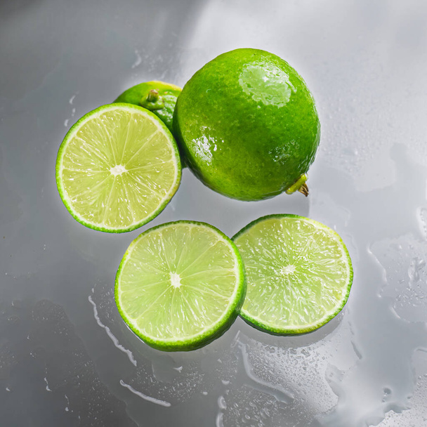 Зеленая лайм пуст с разрезанным ломтиком лайма, показывающим внутреннюю часть мокрой лимонной мякоти на прозрачной стеклянной поверхности, отражая тени лайма и влажной воды, придавая ей свежесть.. - Фото, изображение