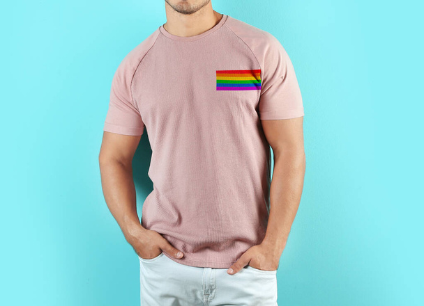 Young man wearing pink t-shirt with image of LGBT pride flag on turquoise background - Foto, imagen