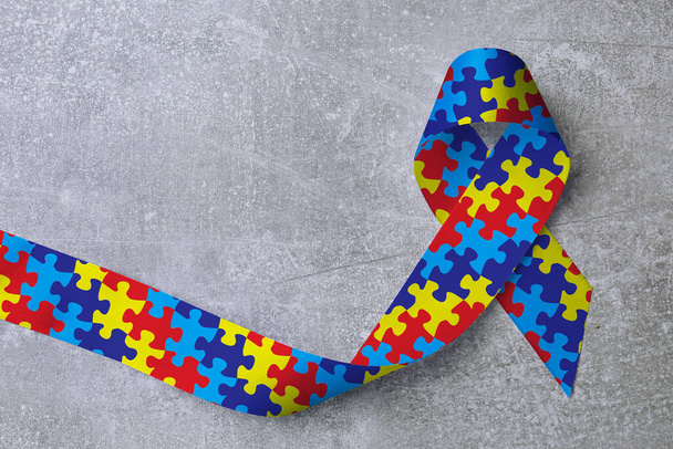World Autism Awareness Day. Colorful puzzle ribbon on light grey stone background, top view - Foto, imagen