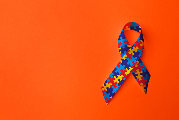 World Autism Awareness Day. Colorful puzzle ribbon on orange background, top view with space for text - Φωτογραφία, εικόνα