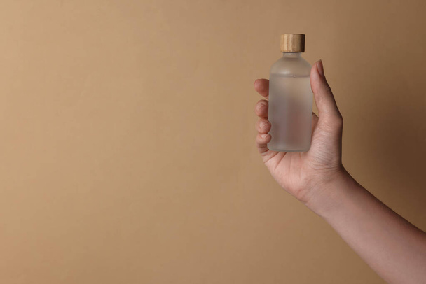 Woman holding bottle of cosmetic product on beige background, closeup. Space for text - Fotografie, Obrázek