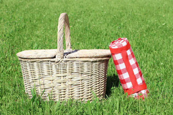 Rolled checkered tablecloth near picnic basket on green grass outdoors - Fotoğraf, Görsel