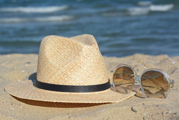 Stylish straw hat and sunglasses on sandy beach - Foto, Imagem