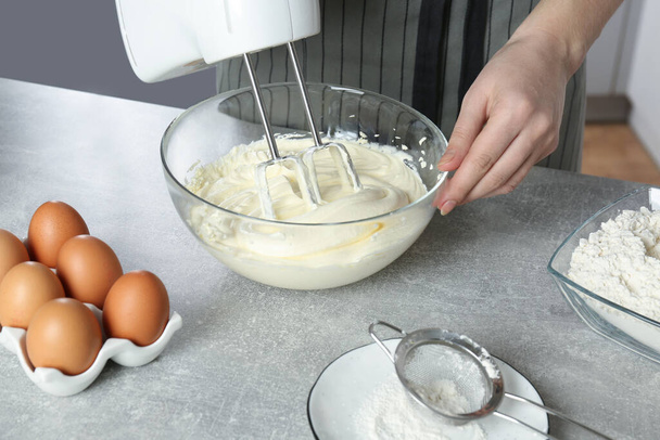 Woman whipping white cream with mixer at light grey table, closeup - Photo, image