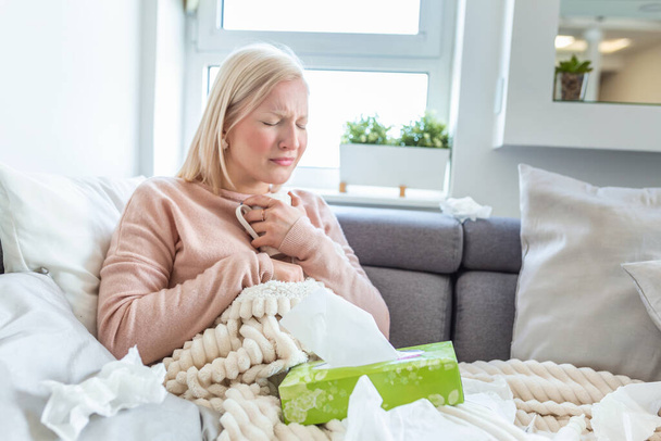 Young woman touching painful neck, sore throat for flu, cold and infection. Unhealthy Girl Covered In Blanket Wiping Nose. Healthcare Concept. Albino girl sick and drinking hot beverage - Foto, imagen