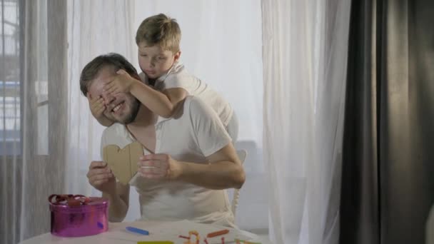 father's day, the son makes a gift to his father for the holiday. Happy family adult parent dad and small son having fun at home  - Séquence, vidéo