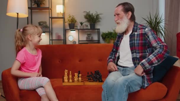 Glimlachende oude grootvader die schaakt met een tienerkleindochter in de huiskamer. Gepensioneerde oudere grootouder geniet van bordspel, rusten met kind meisje kind. Vrijetijdsbesteding voor gezinnen - Video