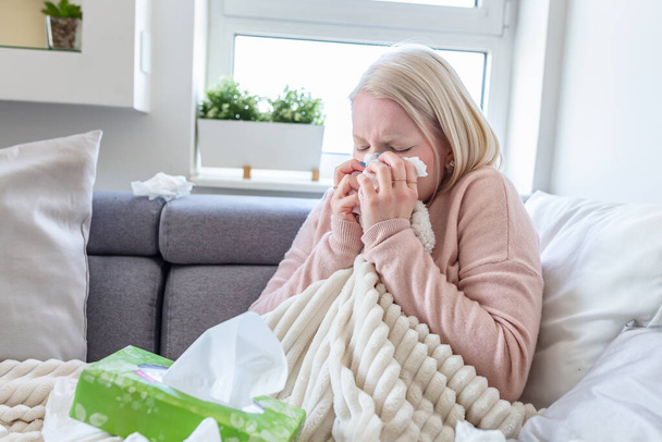 Sick woman with headache sitting under the blanket. Sick woman with seasonal infections, flu, allergy lying in bed. Sick woman covered with a blanket lying in bed with high fever and a flu, resting. - Photo, Image