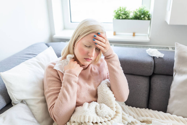 Sick woman with headache sitting under the blanket. Sick woman with seasonal infections, flu, allergy lying in bed. Sick woman covered with a blanket lying in bed with high fever and a flu, resting. - Foto, imagen