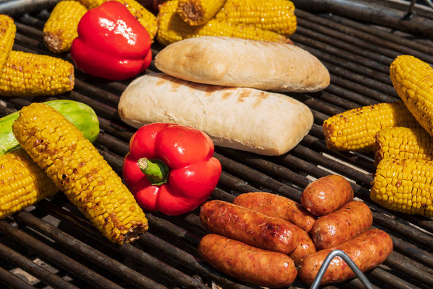 Various snacks on the grill plate. Sausages, corn, red paprika, chiabatta. Tasty picnic food outdoors - Fotó, kép