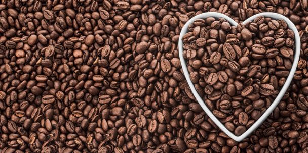 Coffee Beans in White Heart Shape Plate on Fresh Coffee Beans Background with copy space. Flat Lay. High quality photo - Photo, image