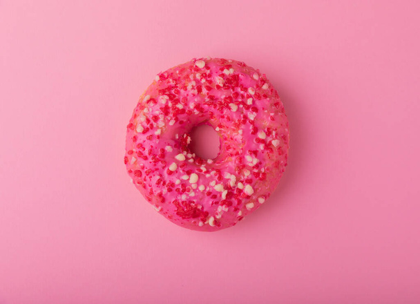 Donut em um fundo rosado.Donut de morango com cobertura rosa e polvilhas em um fundo de papel.Conceito de minimalismo colorido.Junk food.Sweets.Copy space.Flat lay.Place para texto. - Foto, Imagem