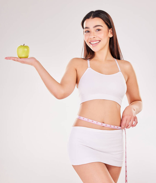 Studio muotokuva viehättävä nuori nainen kädessään omena ja käyttäen mittanauha harmaata taustaa vasten. - Valokuva, kuva