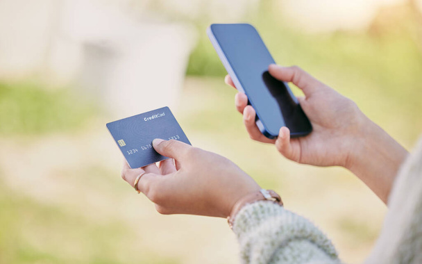 egy nő használja a mobilját, és kezében egy hitelkártya, miközben kint áll. - Fotó, kép