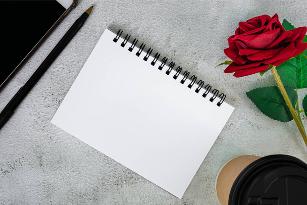 Note book with disposable coffee cup, pen, smartphone and roses on white marble table. Directly above. Flat lay. Copy space. - Foto, Imagen