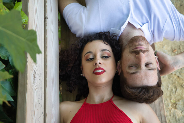 Attractive young couple in love, lying on a bench, heads together and looking into each other's eyes with complicity, seen from above. Concept love, lovers, happiness, valentine's day. - Fotografie, Obrázek