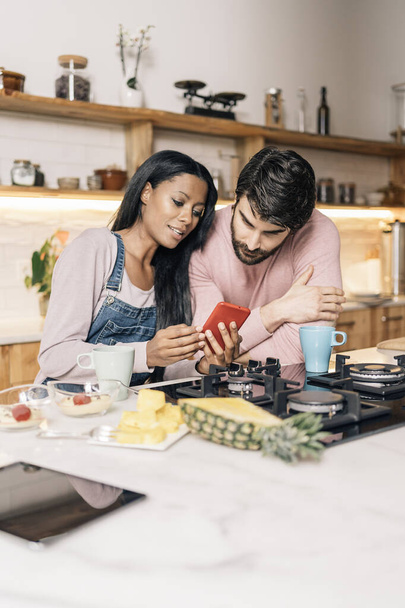 Happy couple having breakfast in the kitchen at home and using phone. - Foto, imagen