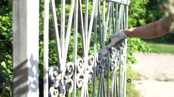 a man paints a gate and a fence. - Video