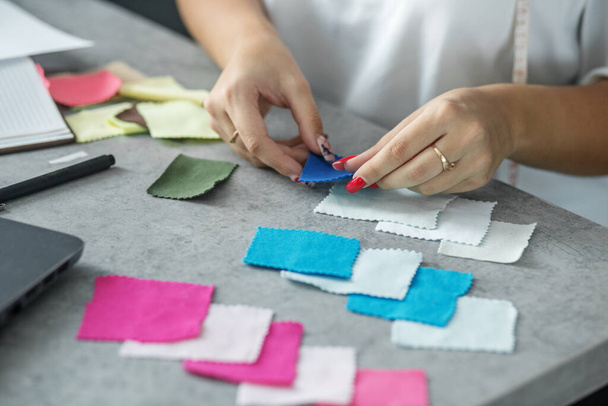 Women's hands hold samples of colored textiles. Fashion designer office. - 写真・画像