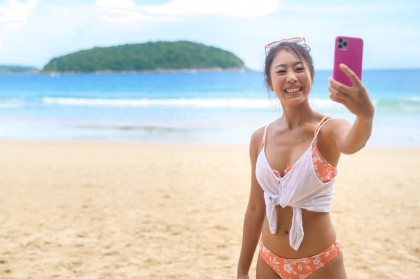 Young Beautiful woman in Bikini listening to music and using smartphone on the beach,  Summer, vacation, holidays, Lifestyles concept. - 写真・画像