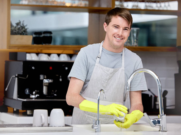 Ένας νεαρός πλένει πιάτα στην κουζίνα του.. - Φωτογραφία, εικόνα