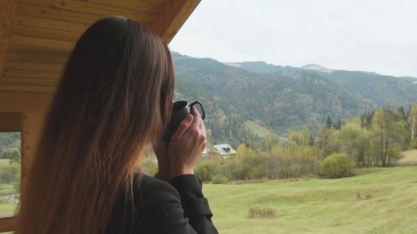 Длинноволосая красивая женщина держит чашку и пьет кофе, чай, смотрит на горы, лес, долину. Облачно, средний выстрел. Феерия, отель, доброе утро, отдых, наслаждение, природа. Высокое качество - Кадры, видео