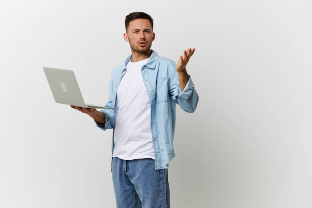 Zdezorientowany, podrażniony, opalony, przystojny mężczyzna w zwykłej koszulce, zszokowany awarią laptopa z gadżetem, udający odizolowanego na białym tle studia. Skopiuj Kosmiczny Baner Mockup. Koncepcja naprawy elektroniki IT - Zdjęcie, obraz