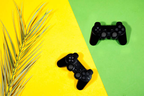 black joysticks, game controller with palm leaf on yellow, green background - Photo, Image