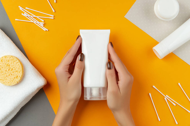 Womans hand holding cream on orange background. Beauty treatment wellness concept. - Photo, Image