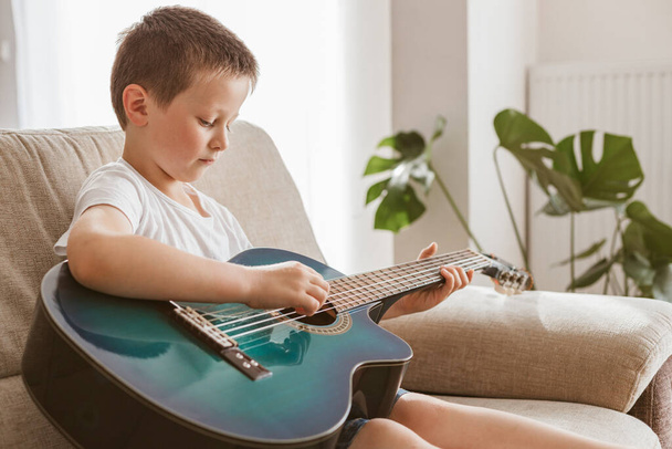 Чарівний маленький хлопчик вчиться грати на акустичній гітарі вдома. Хобі та розваги для дітей вдома
. - Фото, зображення