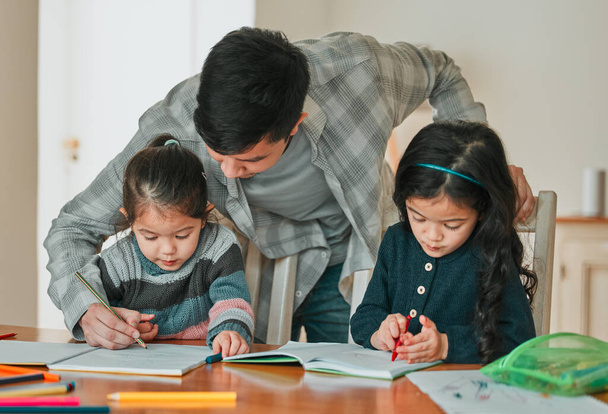 a young father helping his daughters with their homework. - 写真・画像