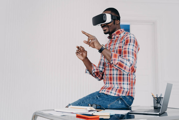 African american student in vr glasses at home. Young businessman has remote virtual study. Afro freelancer is sitting on top of desk. Modern digital technology for business and e-learning. - Fotoğraf, Görsel
