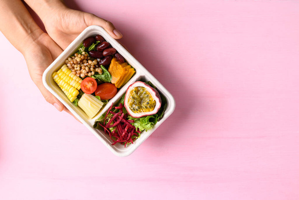 Салат зі свіжих овочів у біорозкладаній мисці з рукою на рожевому фоні, здорове веганське харчування
 - Фото, зображення