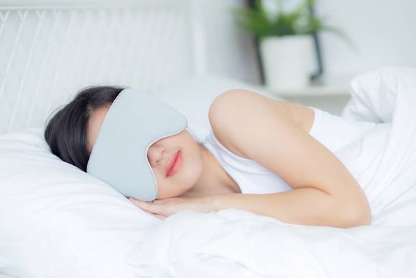 Piękna młoda azjatycka kobieta nosząca okładkę oka i śpiąca na łóżku z głową na poduszce komfort i szczęście w sypialni w domu, dziewczyna z relaksem i wypoczynkiem dla wellness, koncepcja stylu życia. - Zdjęcie, obraz