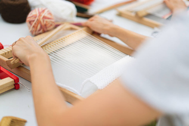 Girl weaving small rug with pattern at masterclass on weaving. Girl is studying how to weave on manual table loom. Process of creation. Handmade concept - Photo, image