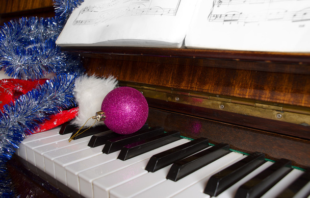 Santa Claus's cap and Christmas decorations lie on a piano. - Photo, Image
