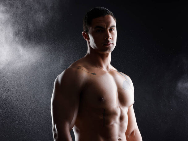 an athletic young man posing shirtless against a dark background. - Φωτογραφία, εικόνα