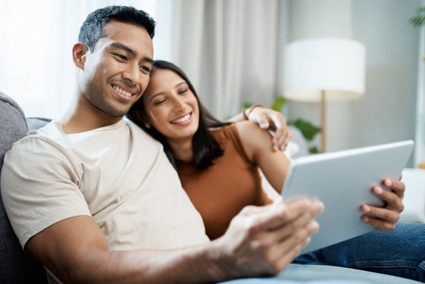 a young couple sitting on the sofa together at home and using a digital tablet. - Foto, imagen