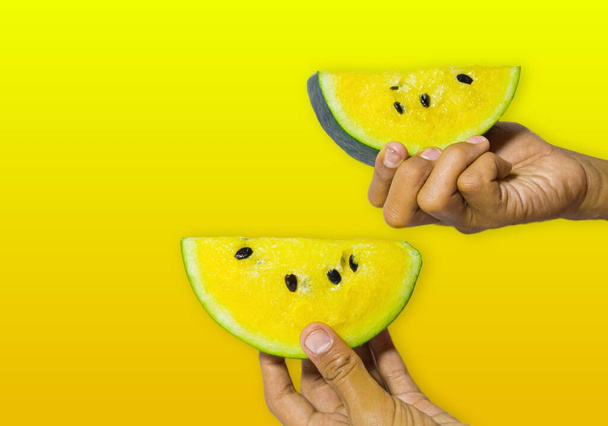 each hand holding a delicious and healthy yellow watermelon isolated on a yellow background. the benefits of watermelon help heart health and there are many nutrients that can nourish the body's skin - Fotó, kép