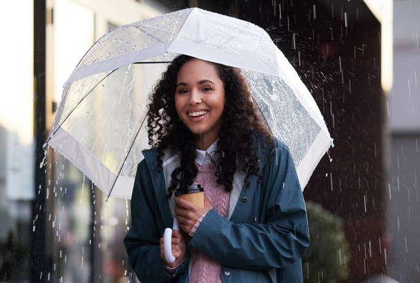 μια νεαρή γυναίκα που κρατά μια ομπρέλα και ένα φλιτζάνι καφέ στην πόλη. - Φωτογραφία, εικόνα