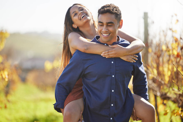 a handsome young man piggybacking his girlfriend on a wine farm. - Foto, imagen