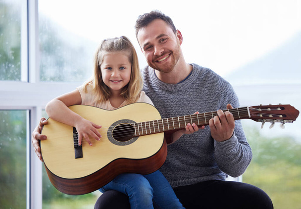 a young father teaching his daughter to play the guitar at home. - 写真・画像