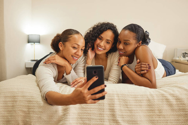 drei Freundinnen machen ein Selfie, während sie zusammen auf einem Bett liegen. - Foto, Bild