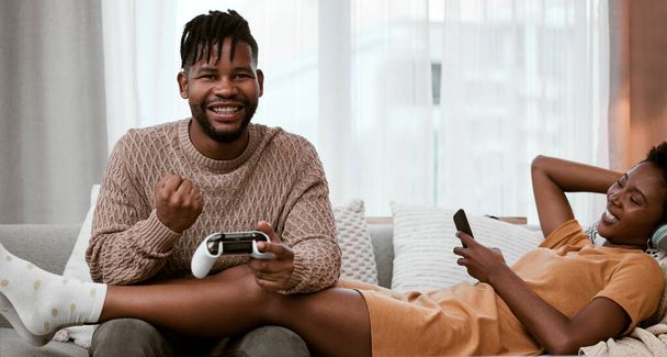 ein hübscher junger Mann spielt Videospiele, während er es sich zu Hause mit seiner Frau auf dem Sofa gemütlich macht. - Foto, Bild