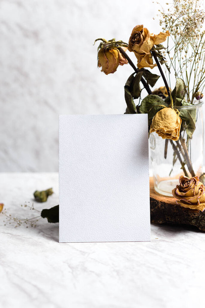 Blank card and wilted flowers on marble background. Concept of nostalgia, breakup, disappointment, separation. - 写真・画像